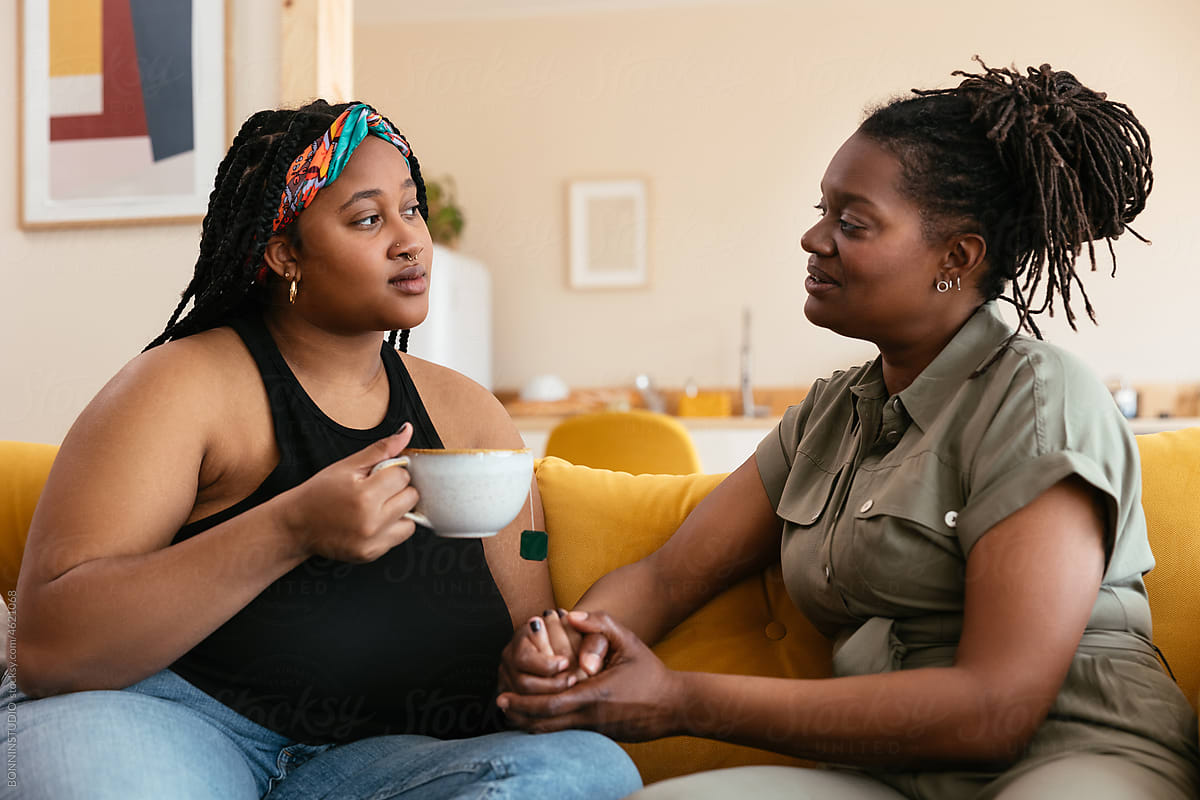 Black mother and daughter with tea speaking on sofa