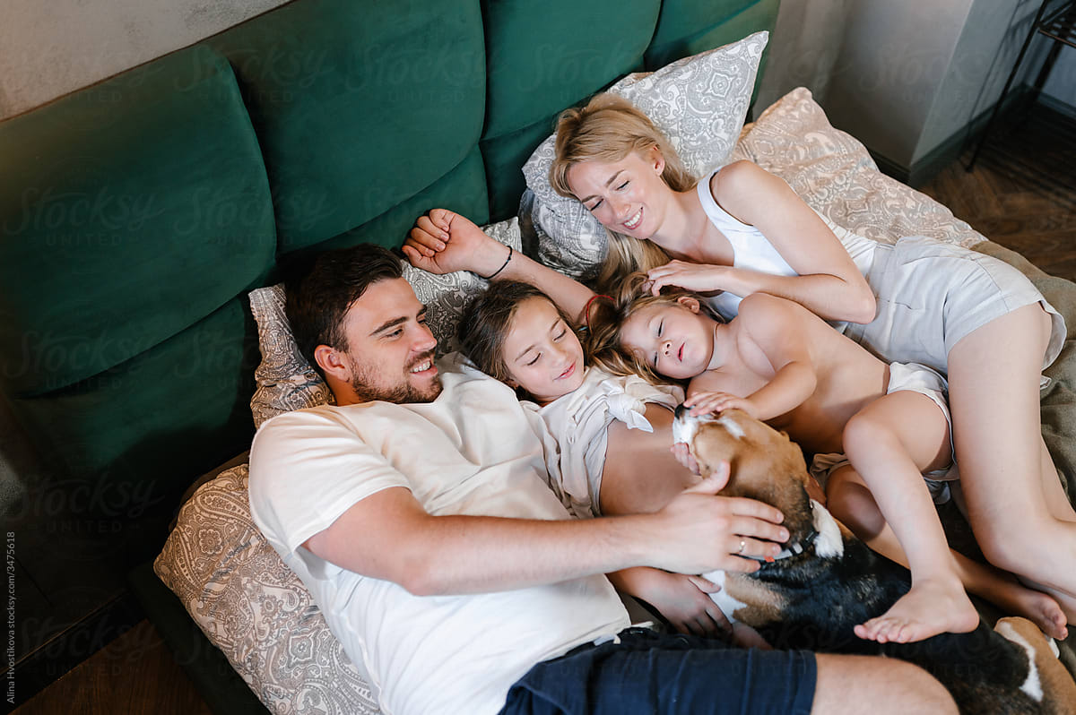 Happy family caressing dog on bed