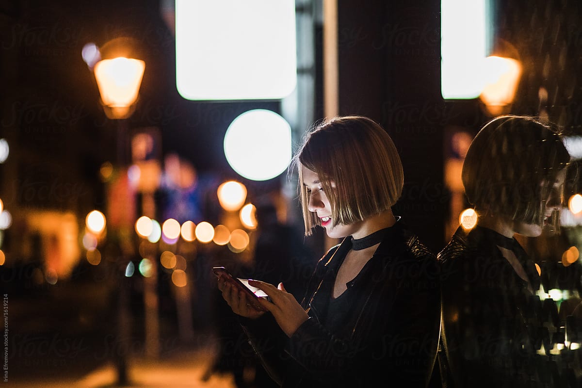 Blond woman with short hair using her smartphone on the street in the evening city.