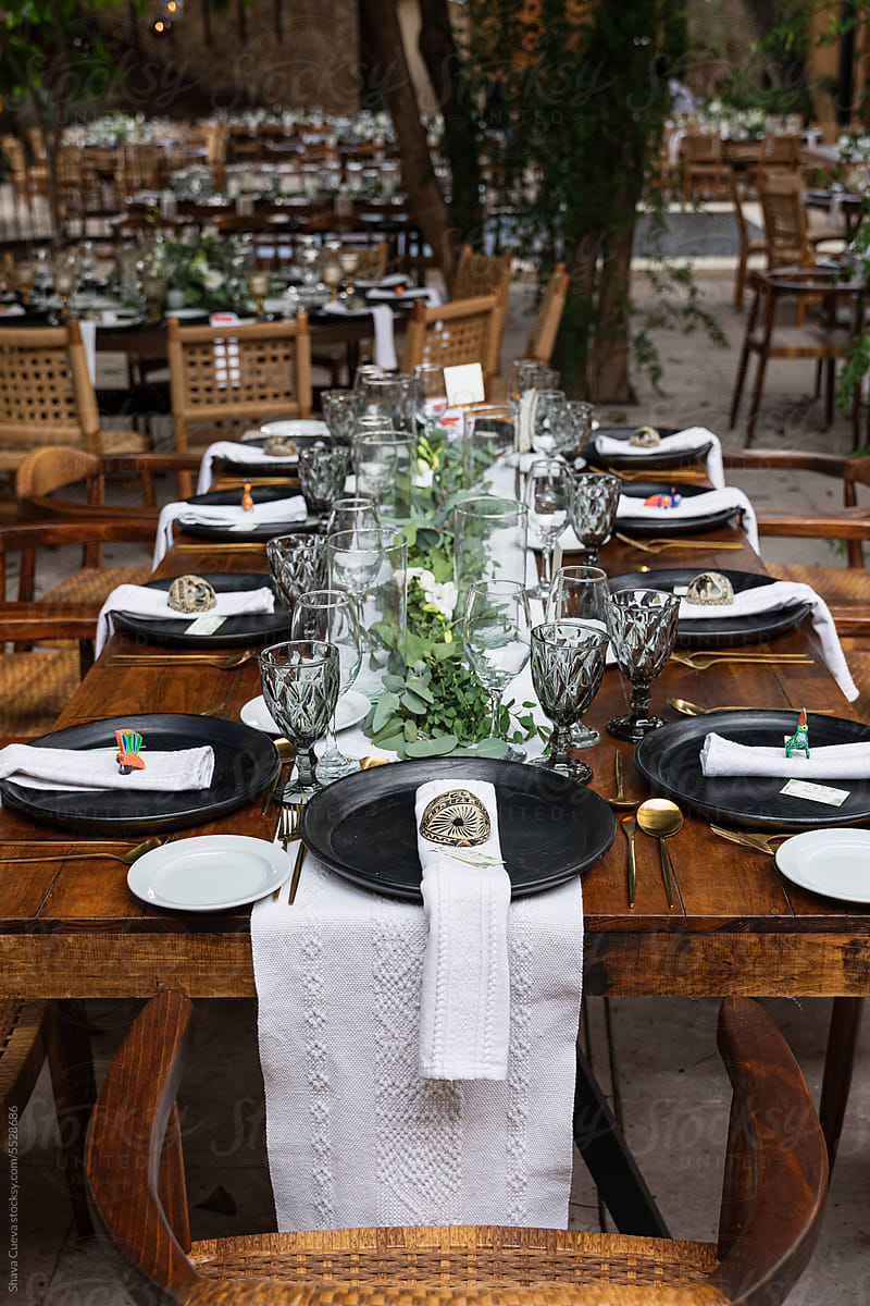 A wooden table with plates and glasses set up for a wedding