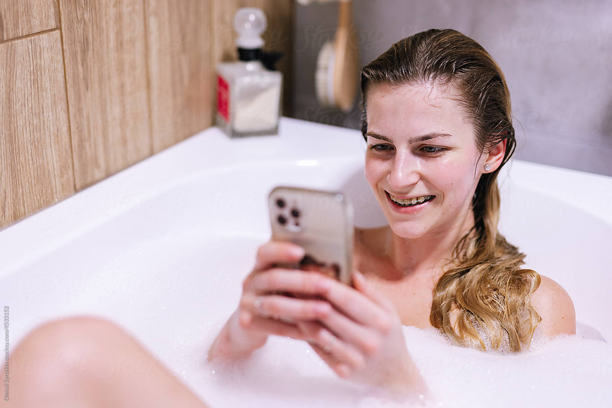 Happy girl using social networking on smartphone in bath