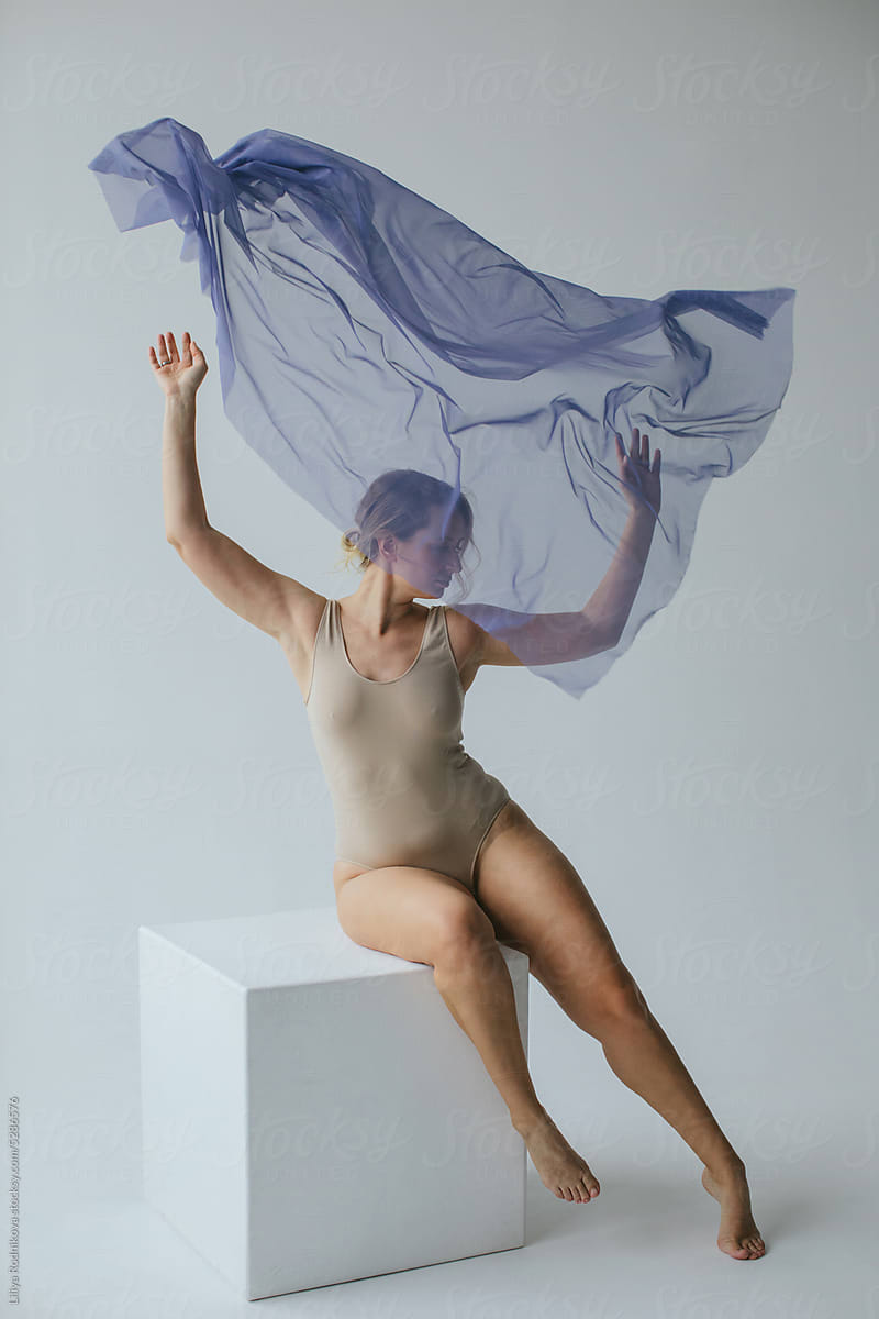 Graceful lady throwing purple material sitting on cube
