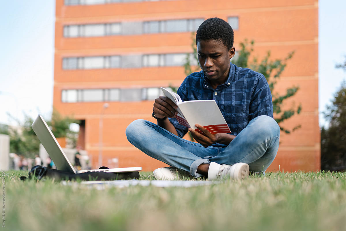 Student reading textbook on park grass