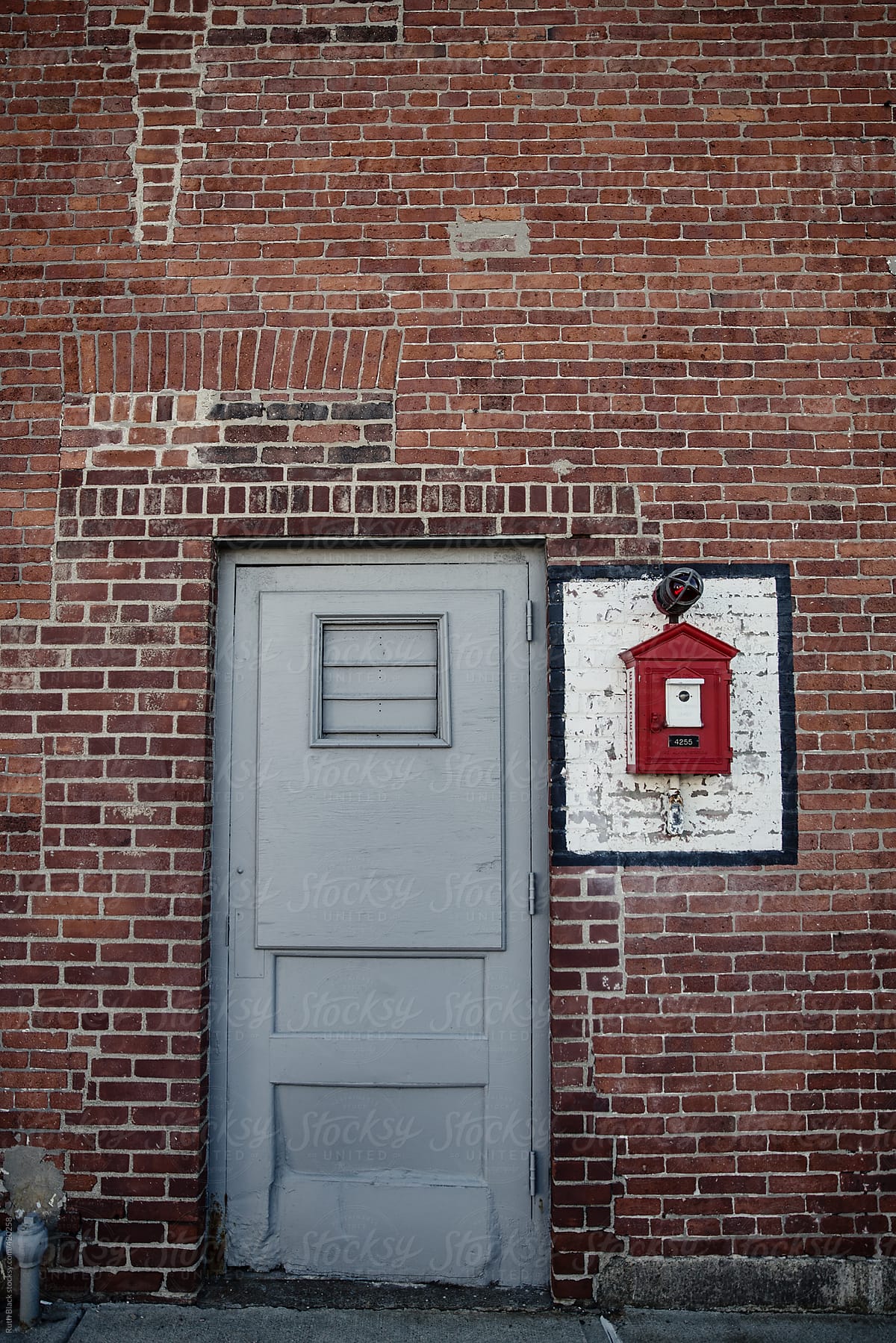 Steel door and vintage fire alarm box on red brick wall