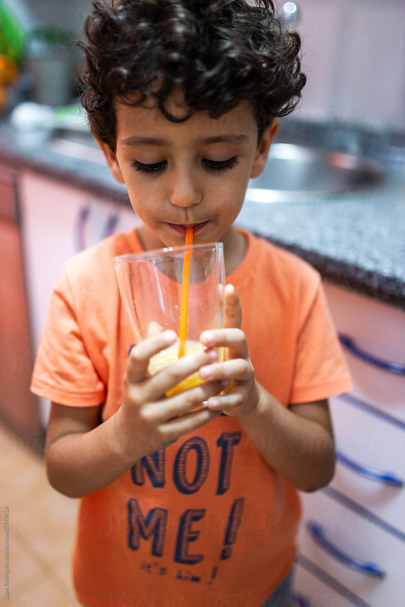curly-haired little boy drinking a fruit juice in the kitchen at home
