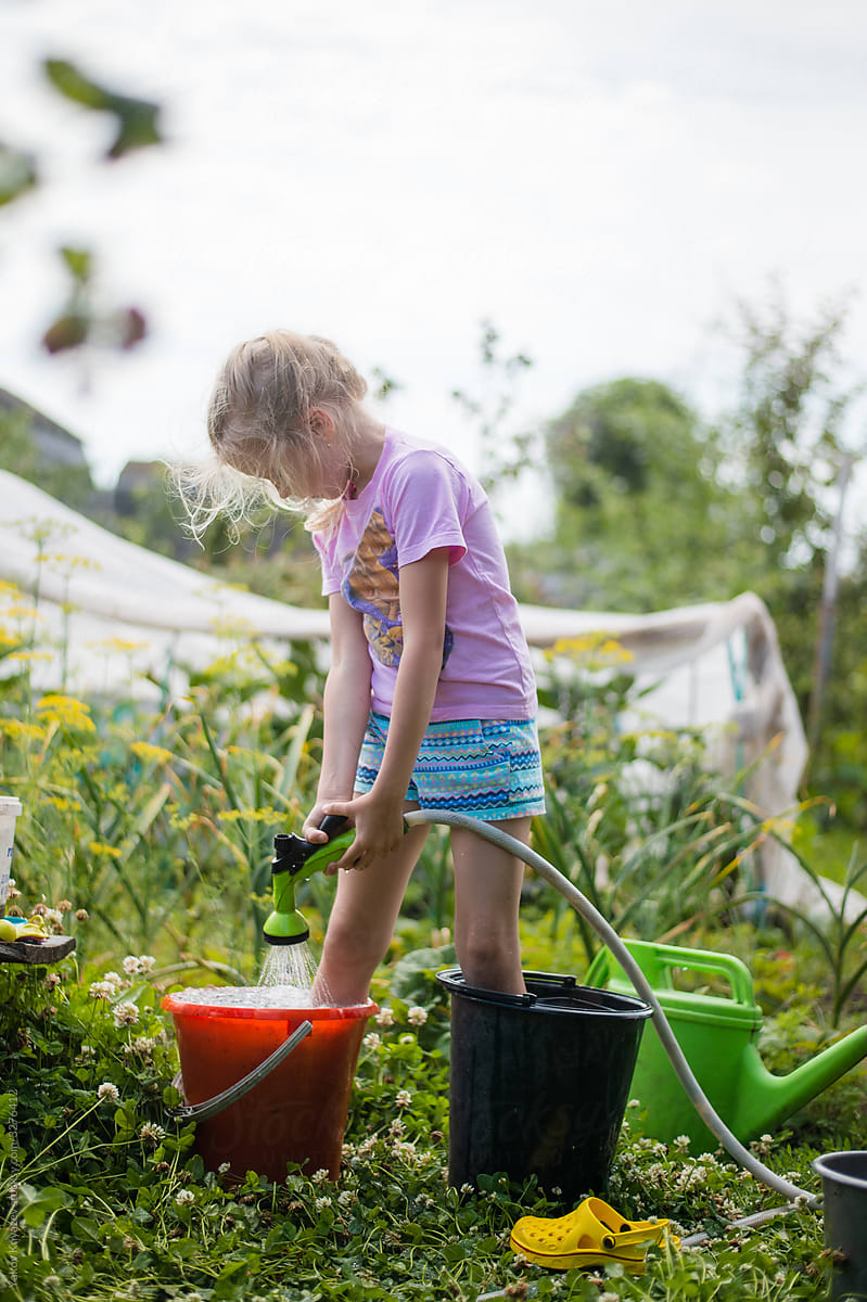 Preschool cute blonde girl watering herself in the garden