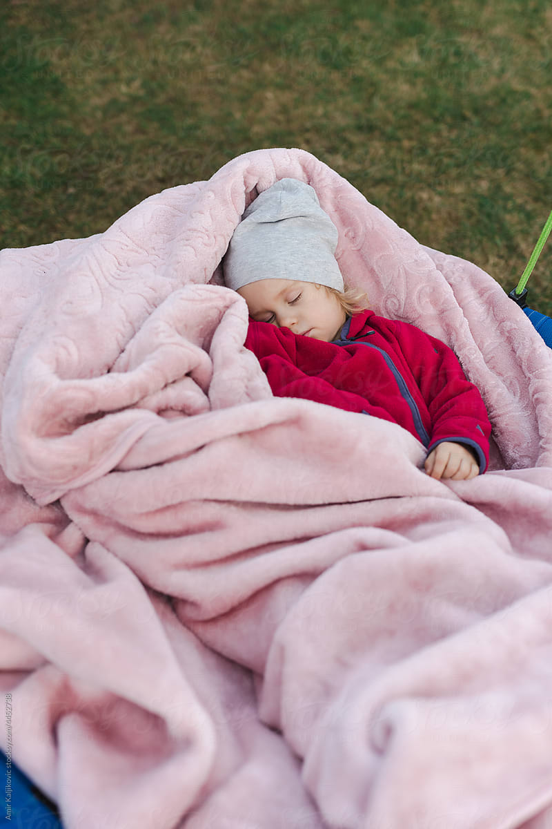 Toddler girl sleeping outdoors covered by a fluffy pink blanket