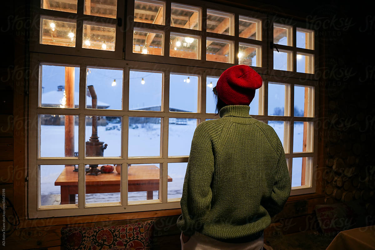 A woman in warm clothes is sitting by the window in winter