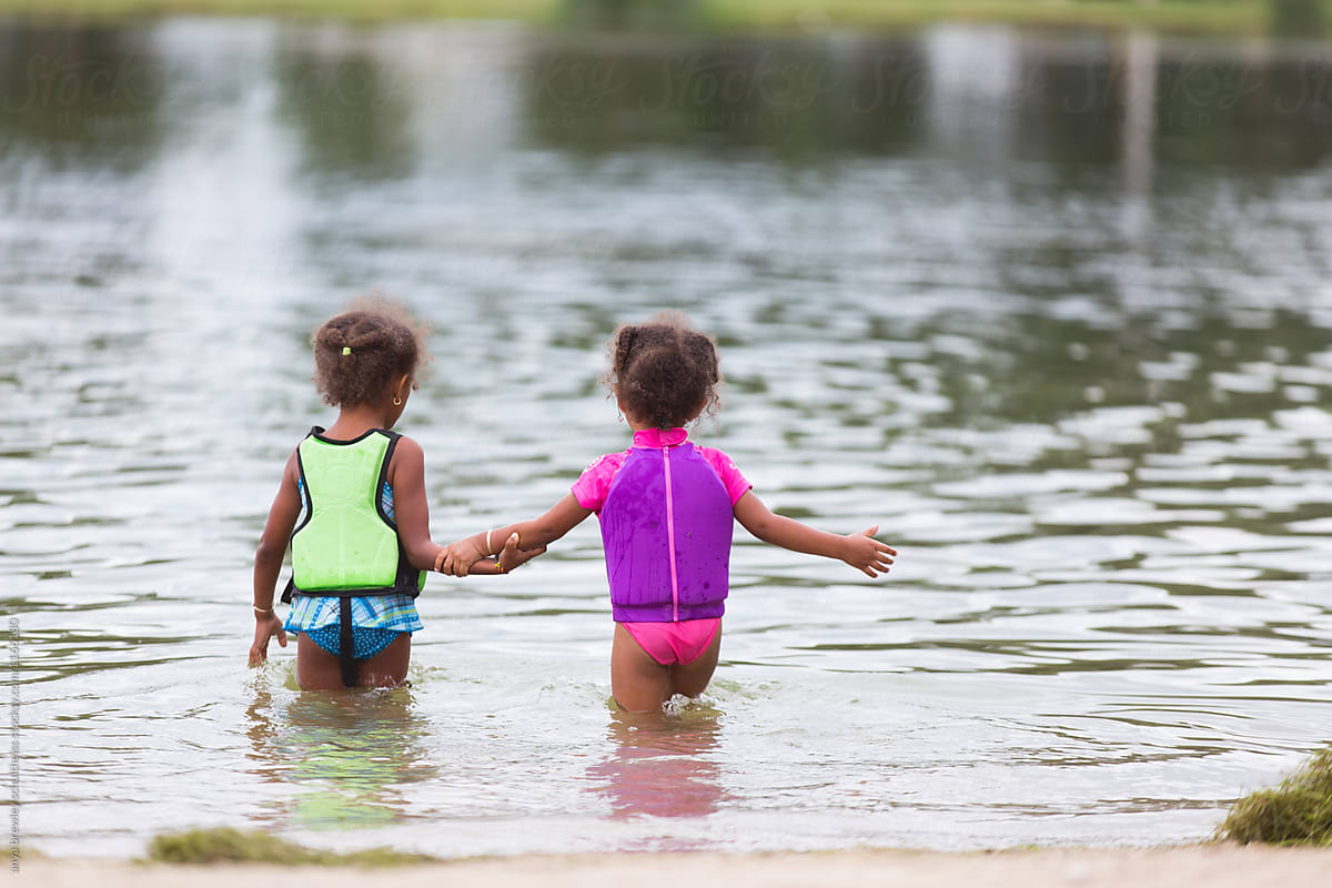 Two Kids In Swim Vests Carefully Wading Into A Lake by Stocksy
