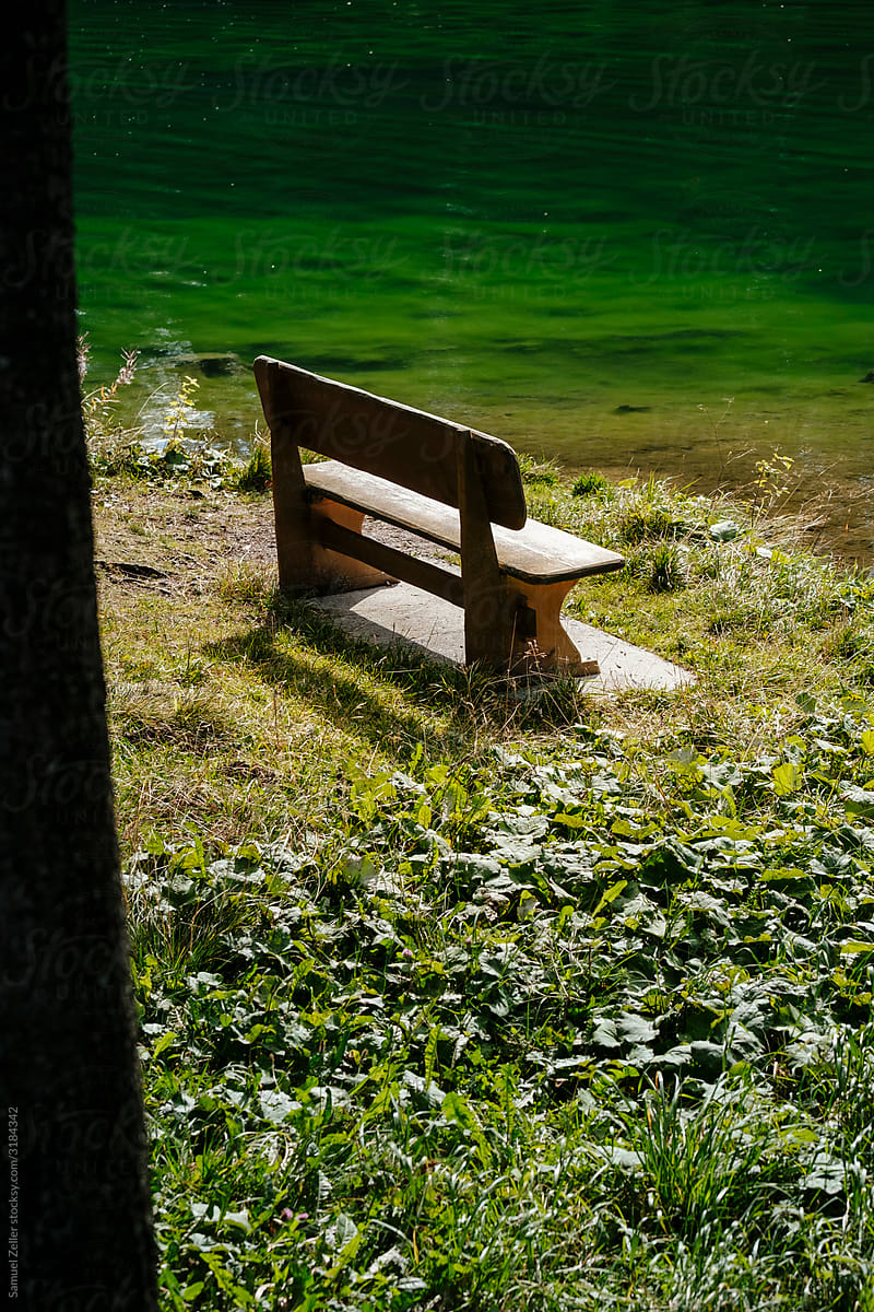 A wooden bench on the shore of a tranquil alpine lake in Lenzerheide, Switzerland