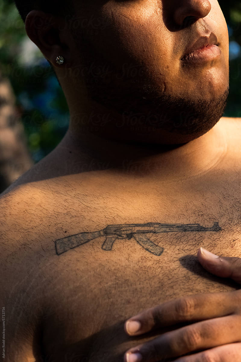 Detail of AK47 shotgun tattoo on the chest of a plus size black boy.