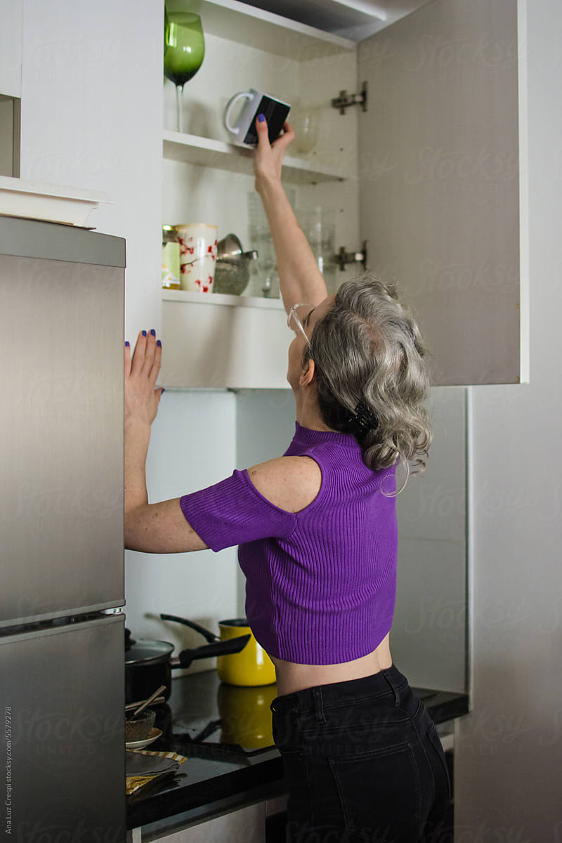 Woman reaching for mug in small tidy kitchen