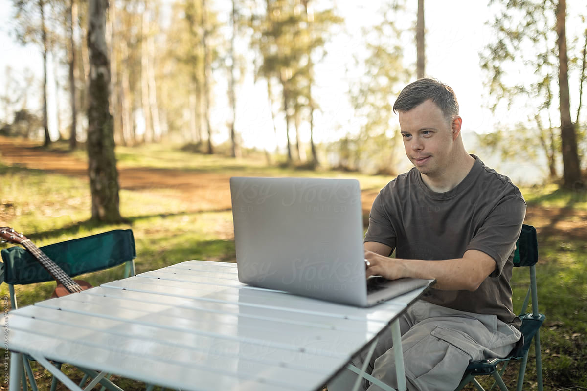 young man with down syndrome using a laptop in nature