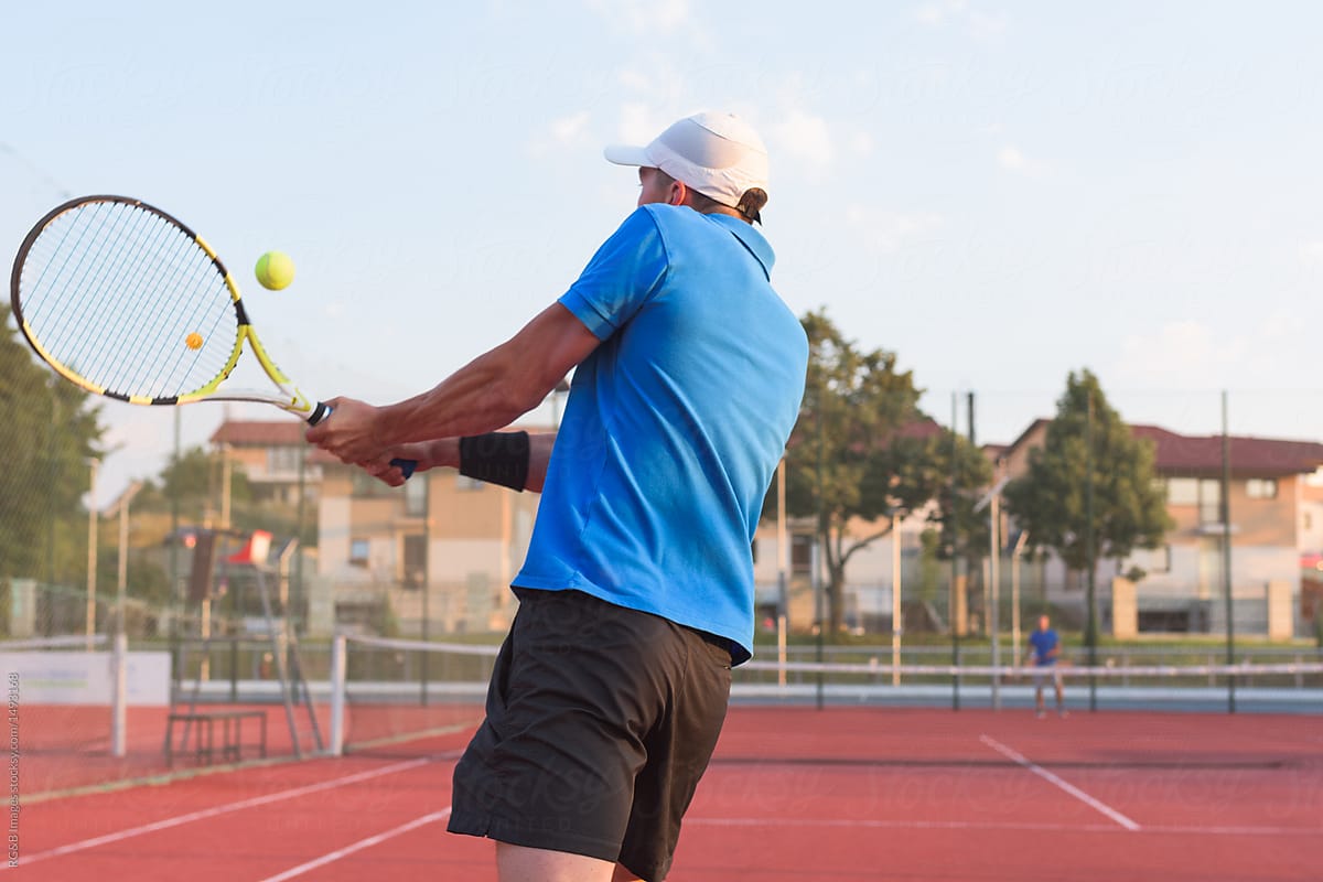 Back view of male tennis player hitting the ball