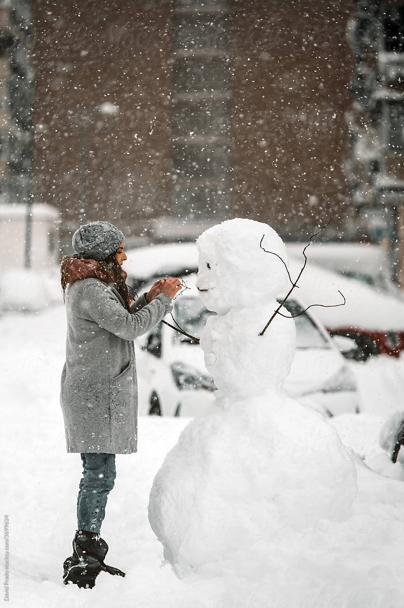Woman making snowman in yard in city