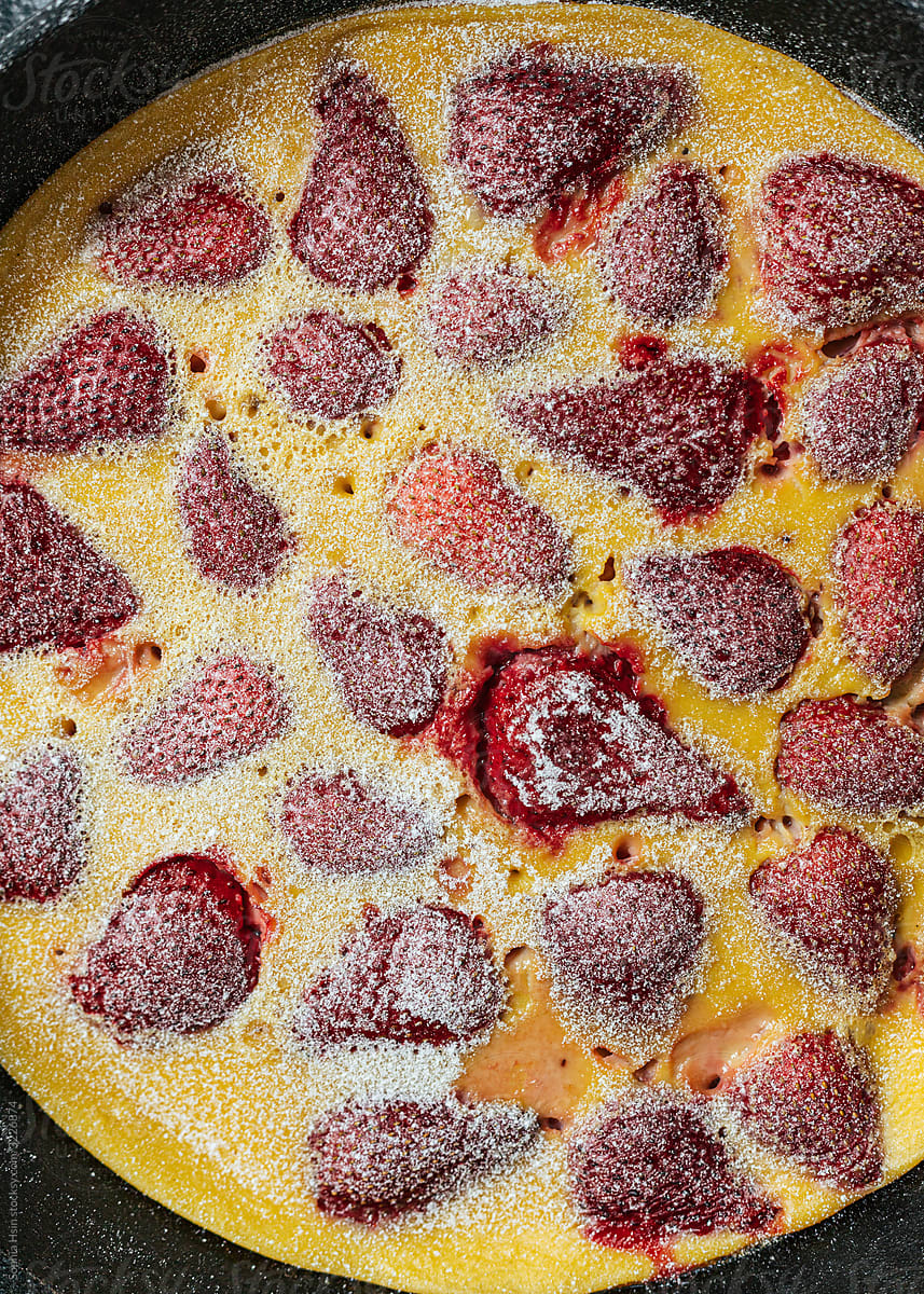 Strawberry clafoutis with powdered sugar in cast iron pan