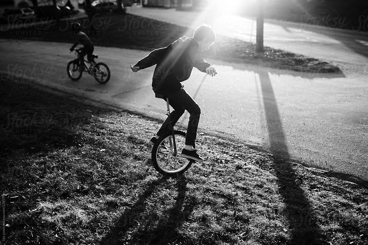 stock photo of boy on  his unicycle  and little brother on bike