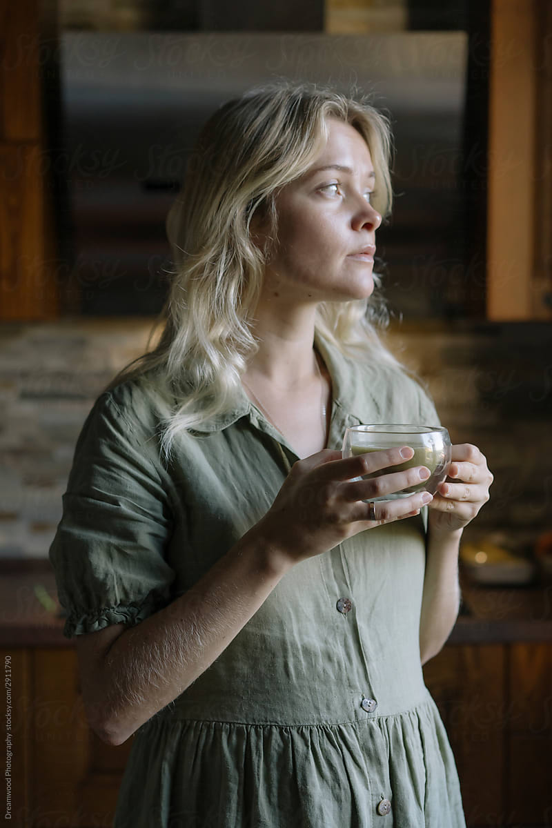 Pensive woman drinking matcha tea at home