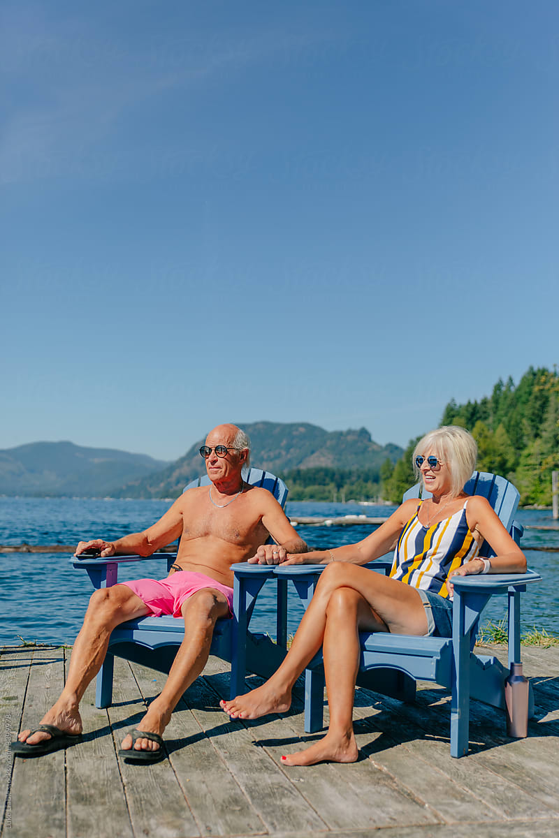 Happy elderly fit couple sitting in swimwear on dock