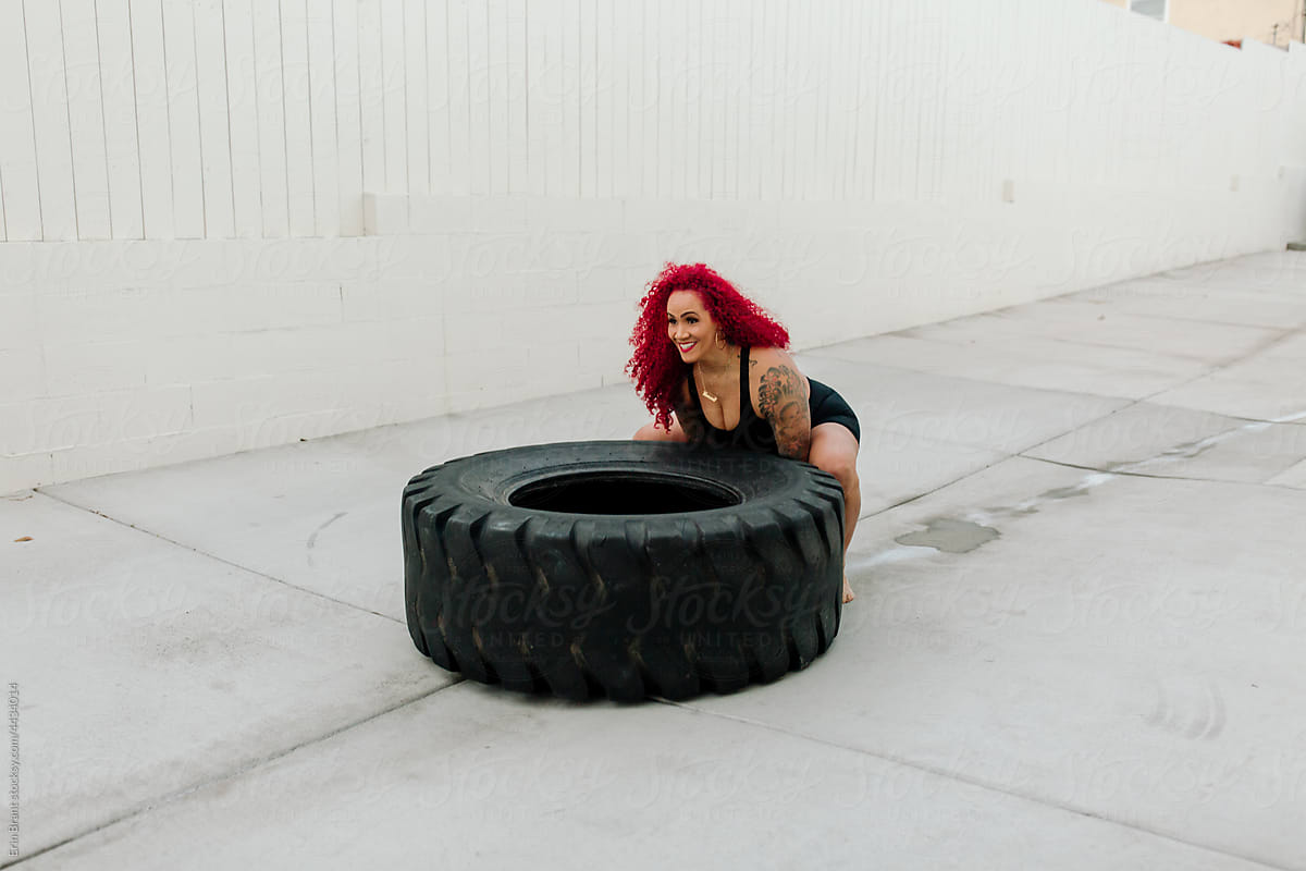 Strong redheaded woman lifting heavy tire