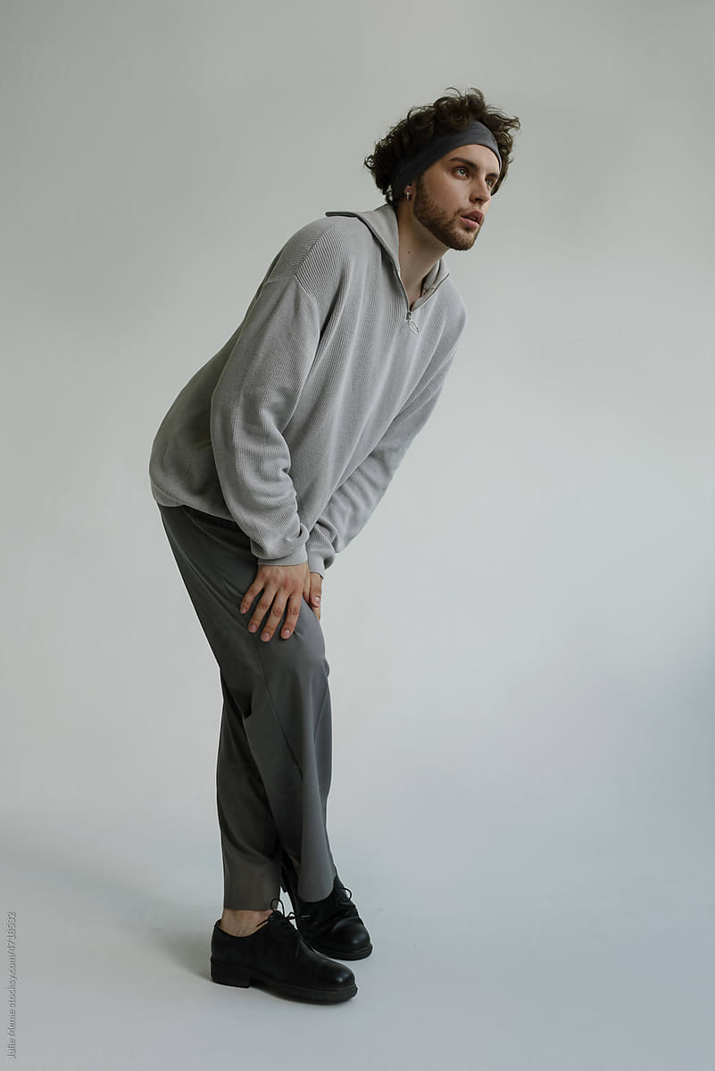 A man in a casual grey outfit stays on a neutral background