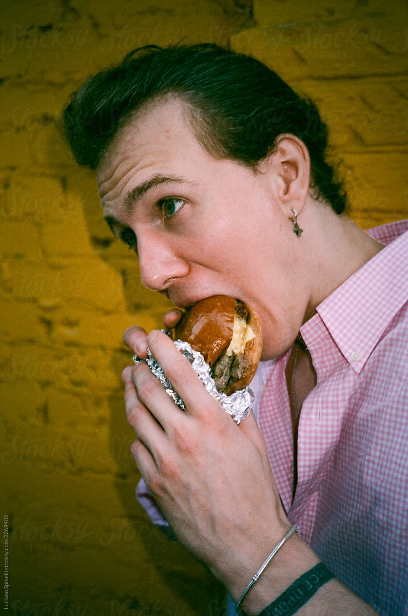 Man in a pink shirt biting burger