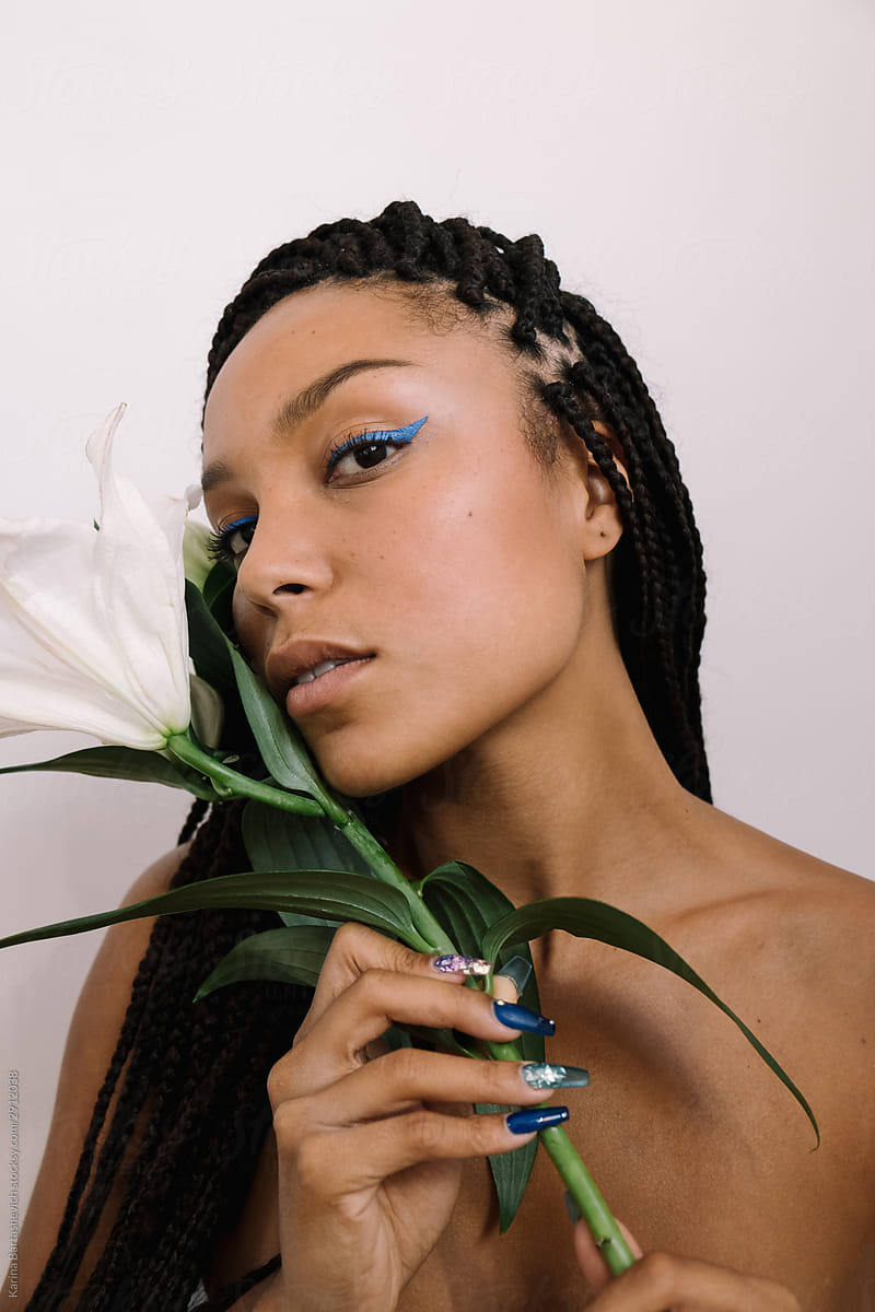 portrait of a dark-skinned girl with pigtails and beautiful collarbones gently holds a lily flower near her face