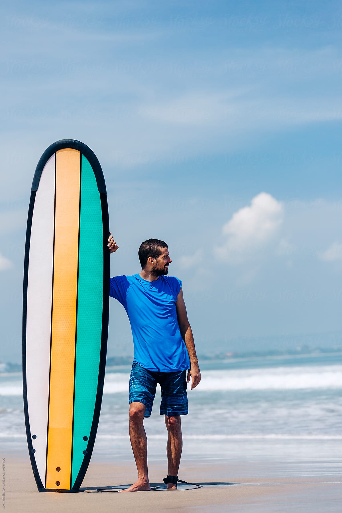 Young surfer standing next to a longboard at a surfing beach