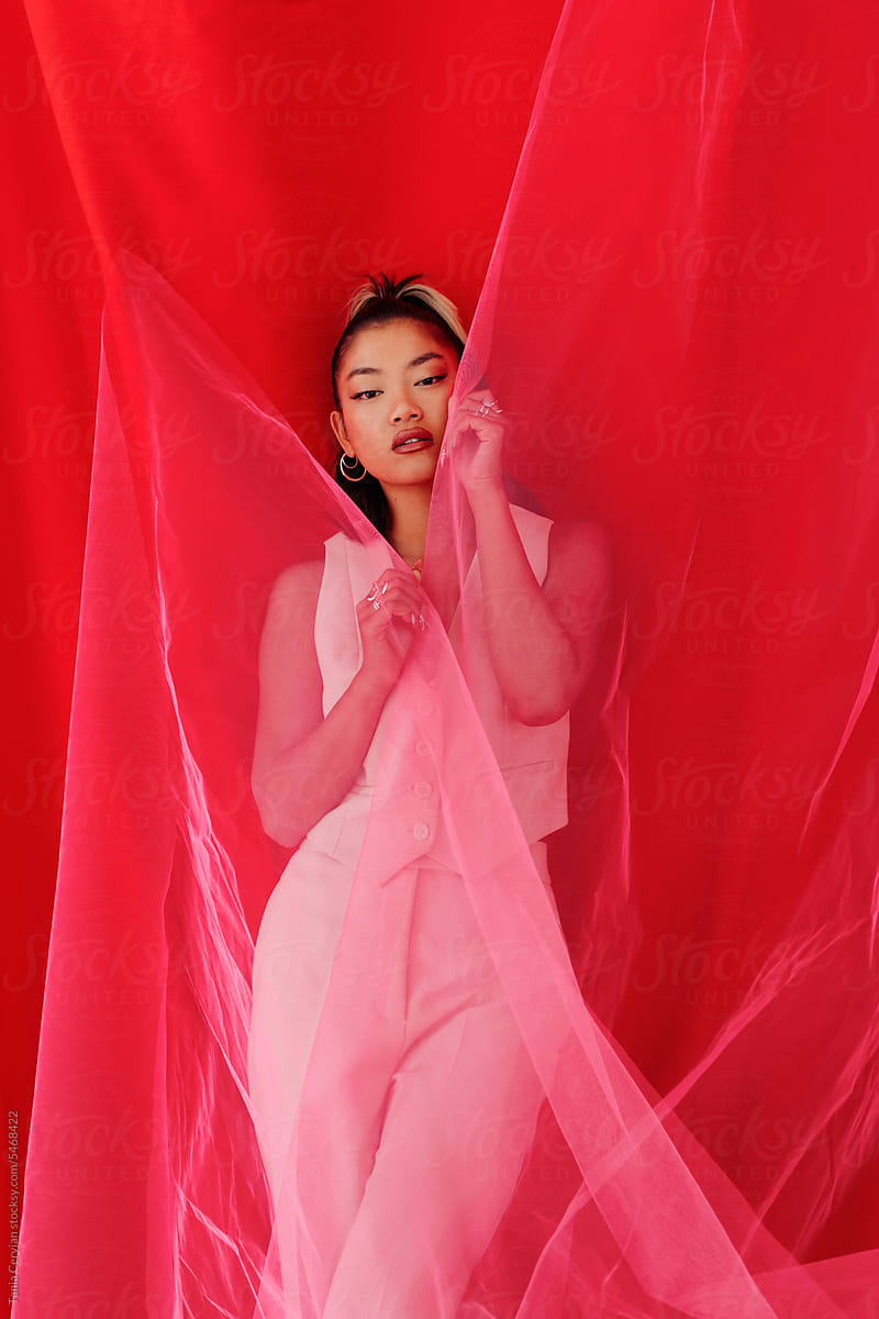 Stylish Asian woman covered in red flowing curtain