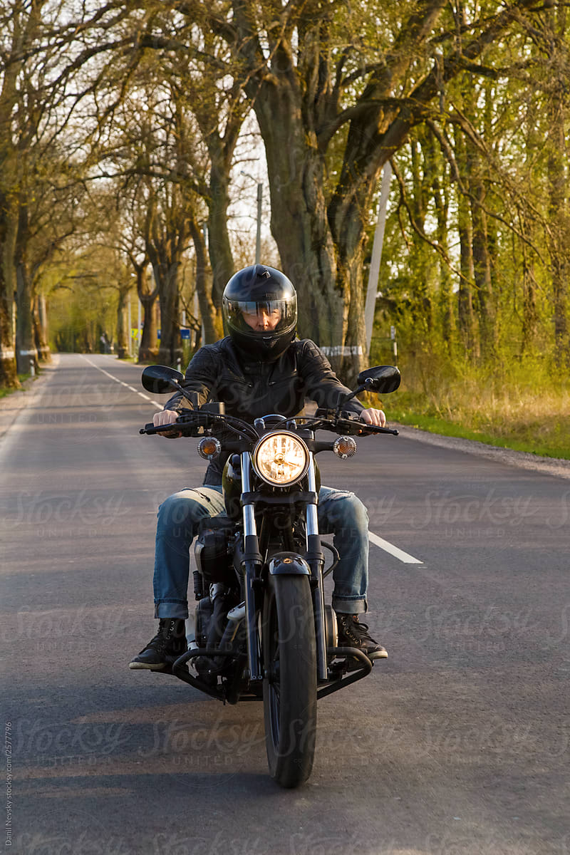 Man riding motorbike through tree avenue