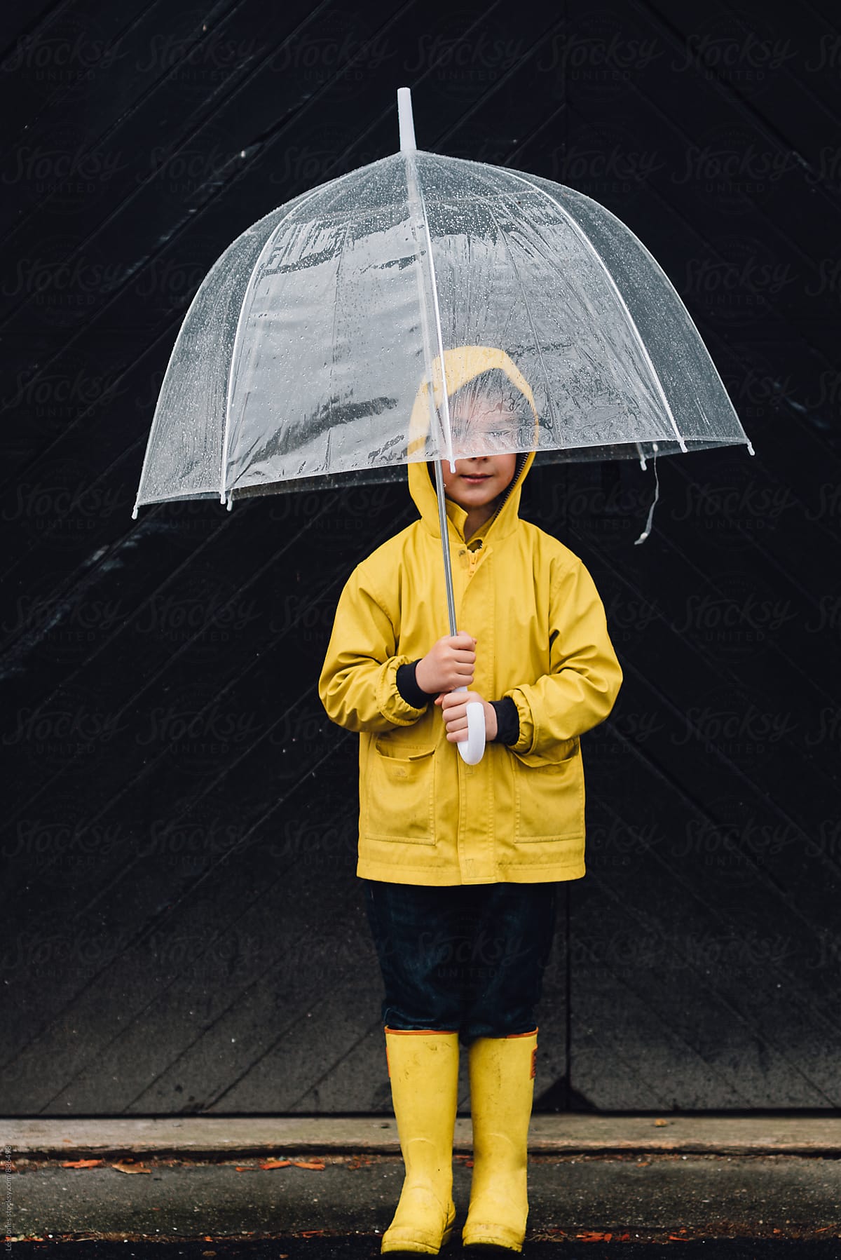 little boy standing in the rain with umbrella
