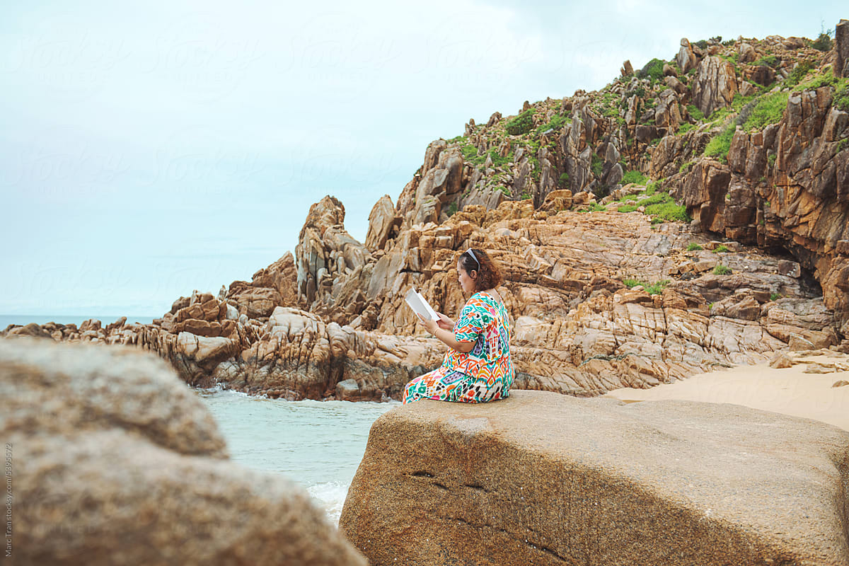 Young woman sitting on rock while reading book at beach