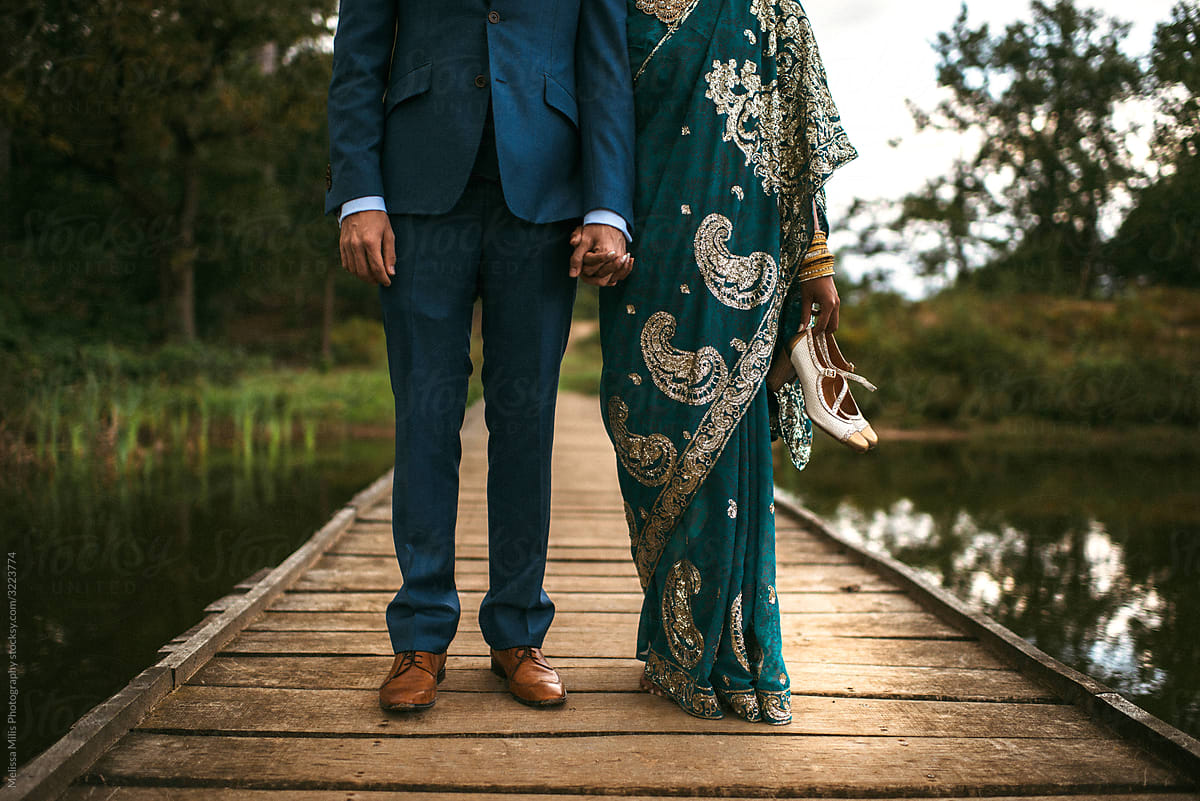 Indian bride and groom holding hands. Bride bare feet with shoes in hands