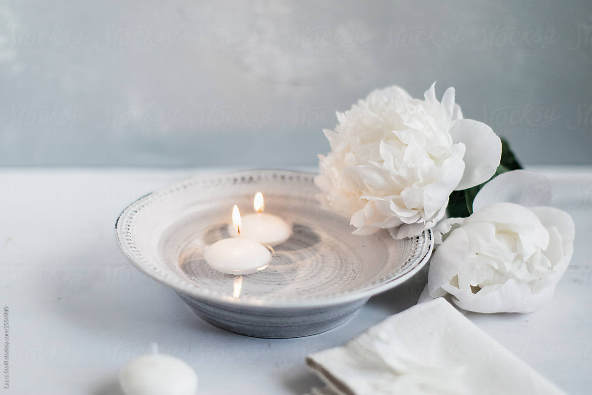 Burning little candles inside porcelain bowl filled with water close to fresh flowers