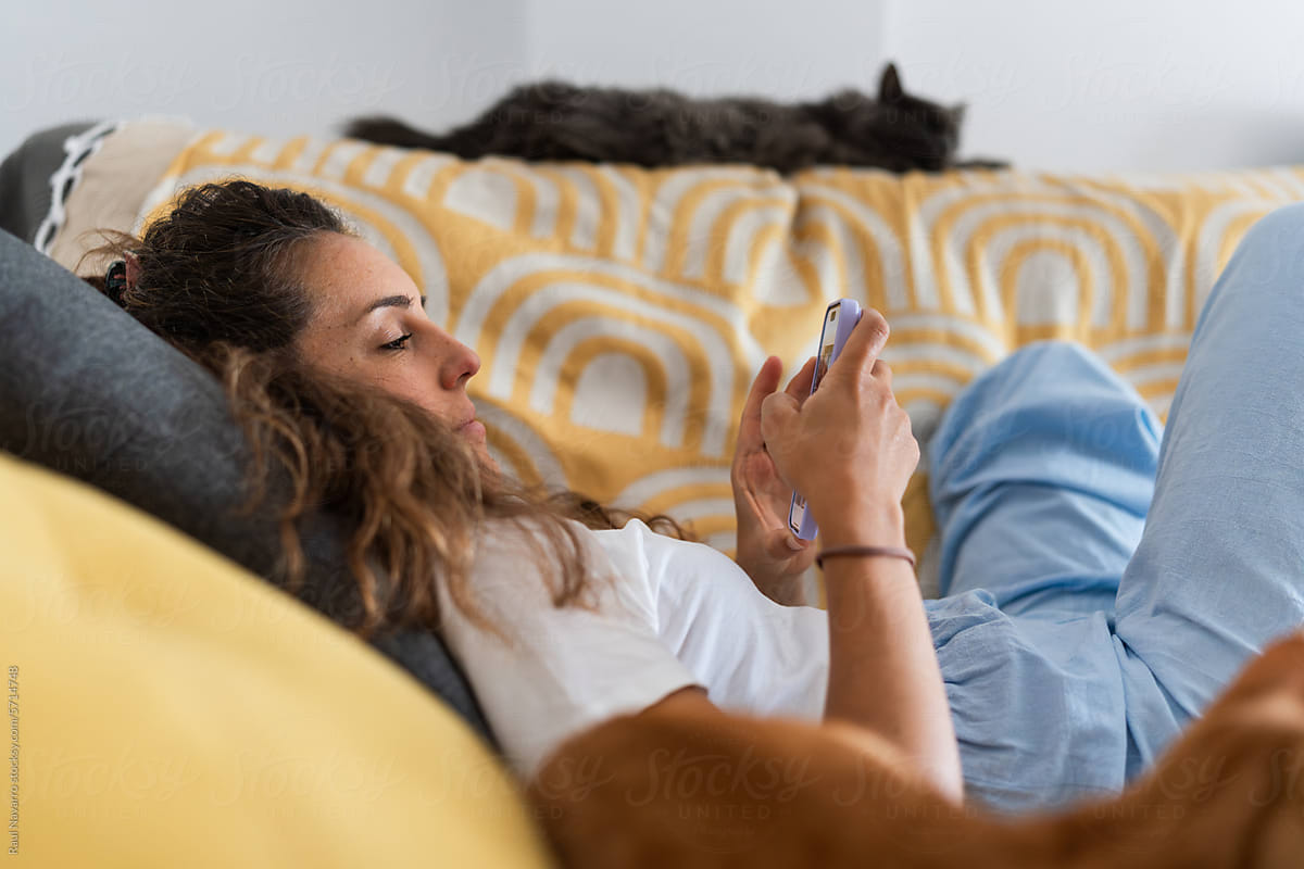 woman using a cell phone lying on the sofa at home.