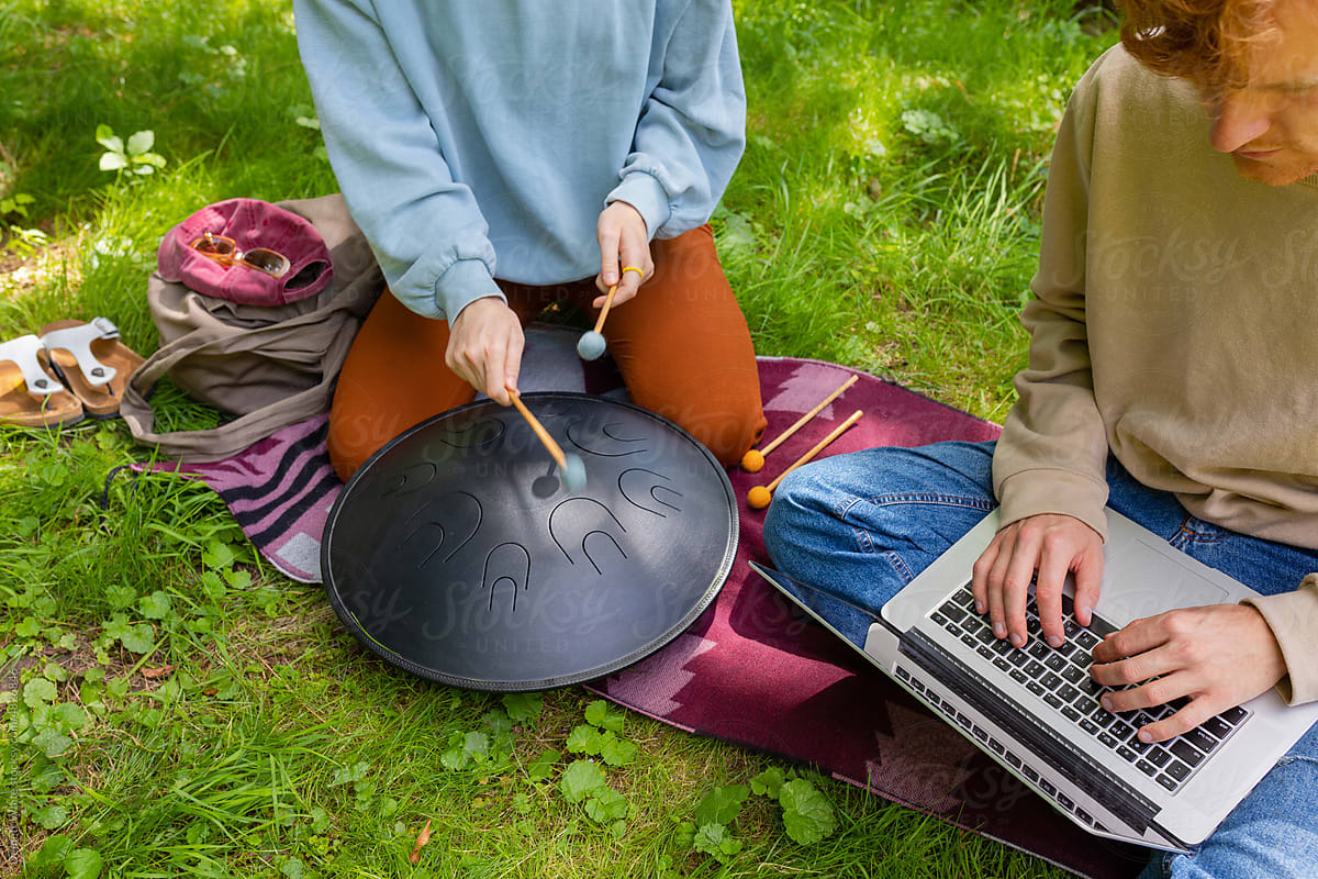 a girl plays a handpan, and a man plays a laptop