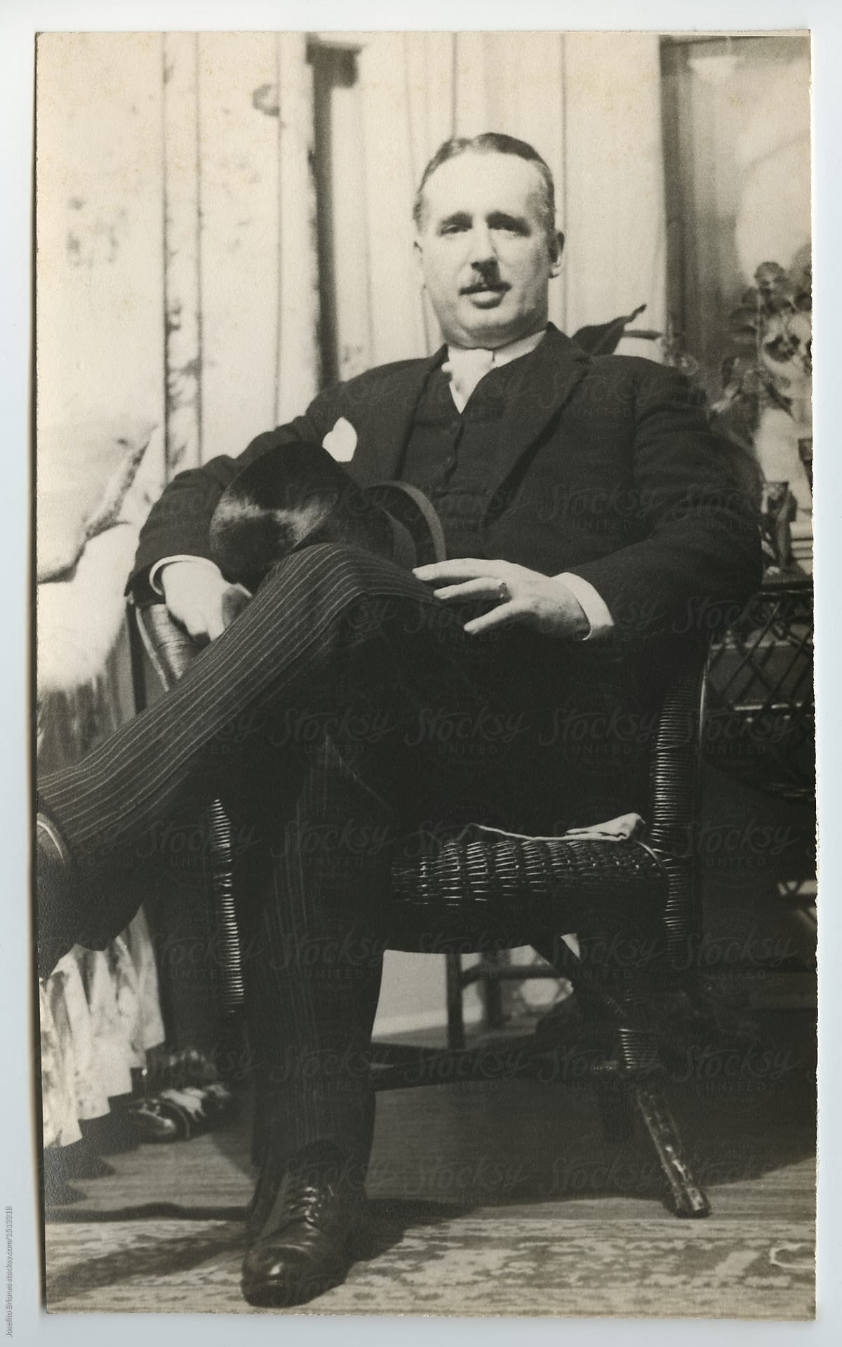An elegantly dressed man sitting in a wicker chair and holding a