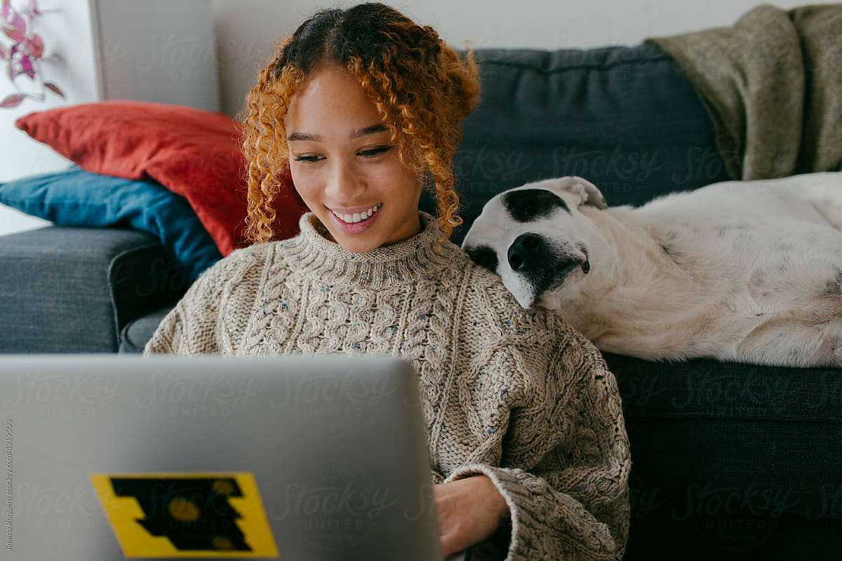 Smiling pretty girl at home with laptop and sleepy dog