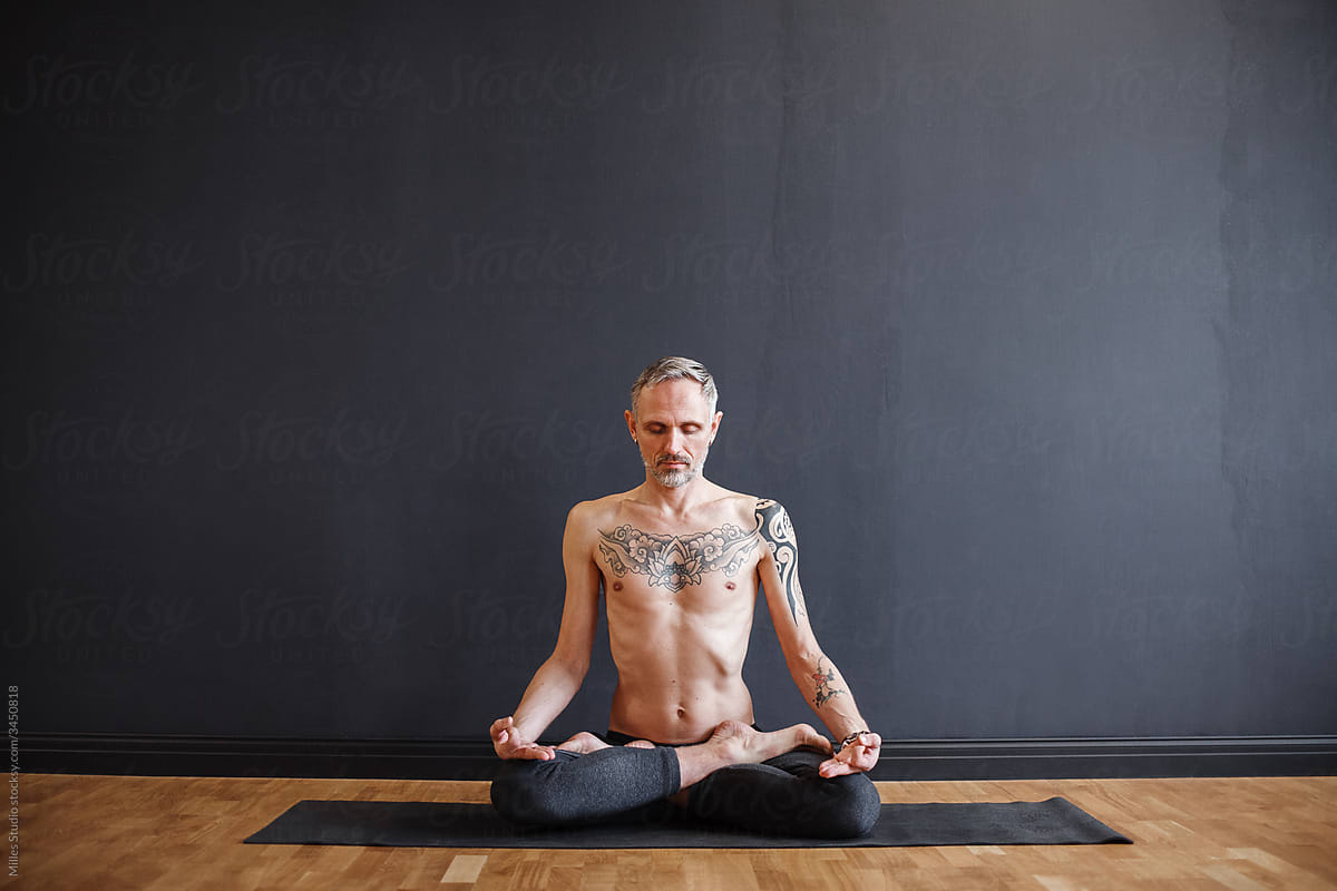 Shirtless male meditating against black wall