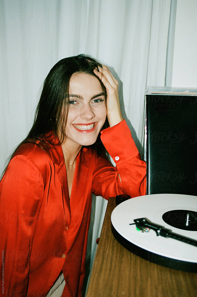 Woman in a red shirt is sitting next to a vinyl record player.