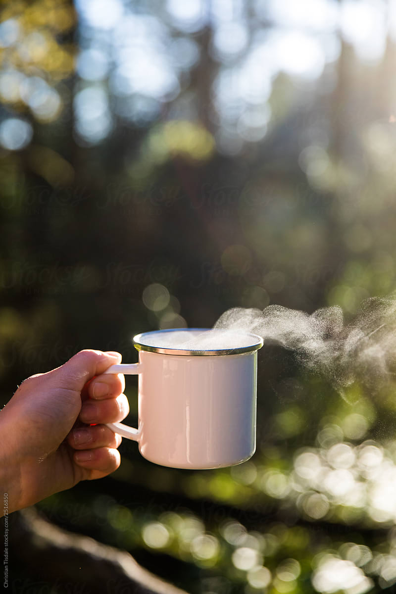 Blank white enamel coffee mug held by a hand in the forest