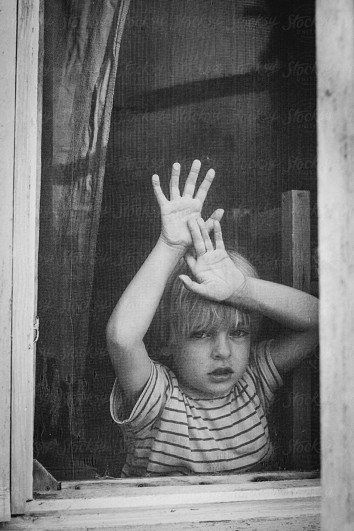 Boy looks out of an old wooden window.