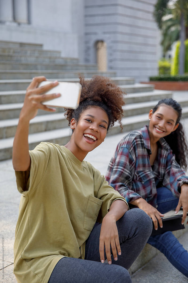 High school girl taking selfie on smart phone  with friend on stairs