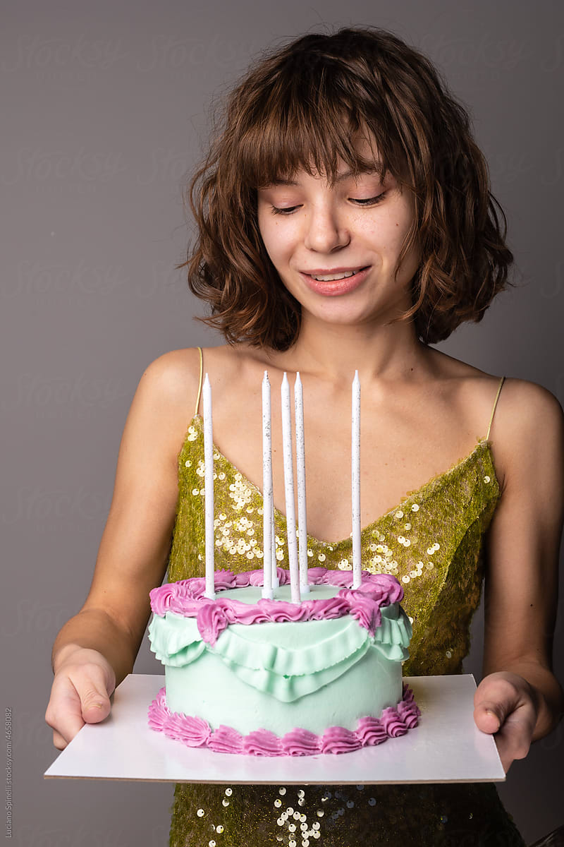 Curly woman in green dress holding a birthday cake with long candles