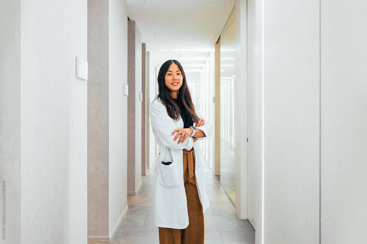 Smiling Asian woman doctor standing in hallway of clinic.
