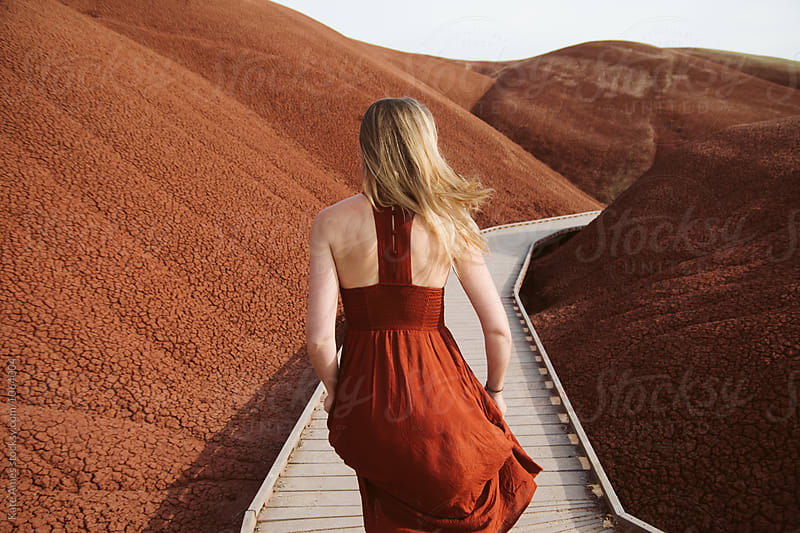 Young woman in red dress running through red painted hills.