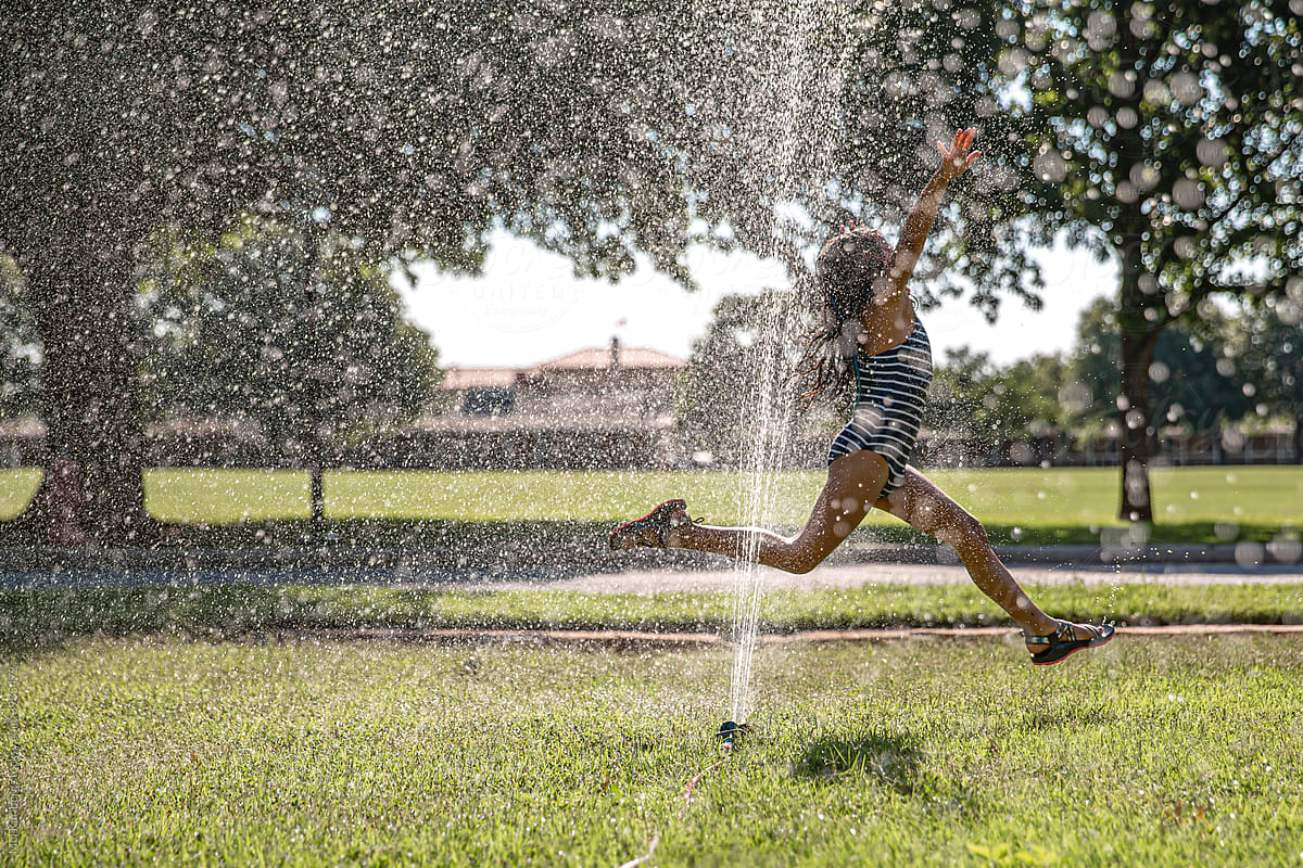 Young girl jumping through a sprinkler