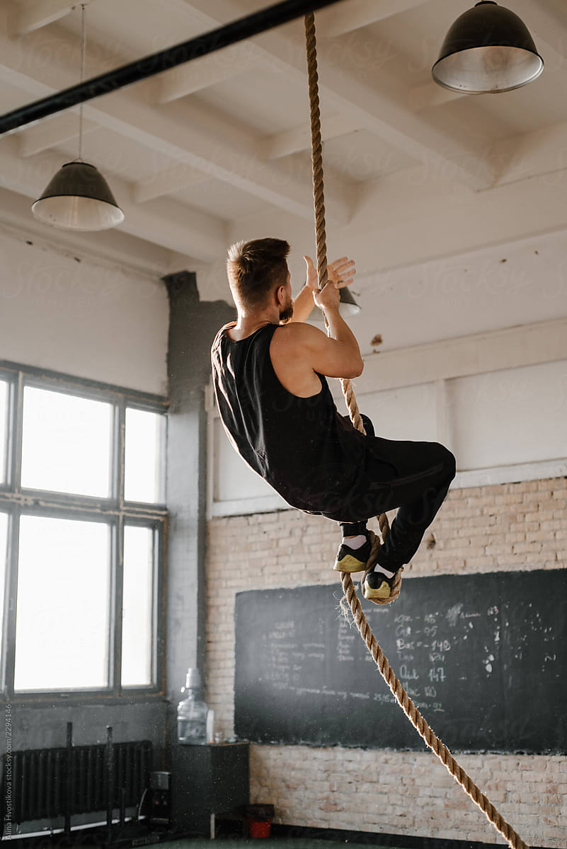 Man Climbing Up Rope In Gym by Stocksy Contributor Alina