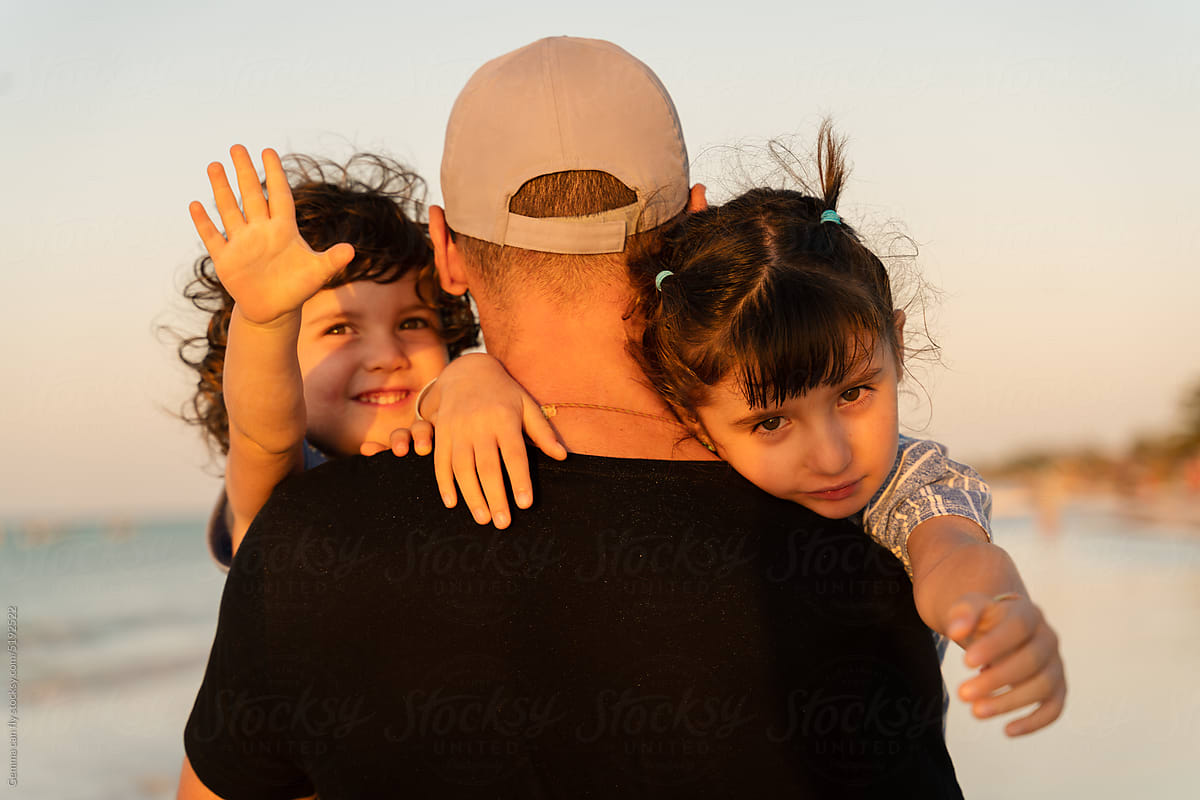 Father holding happy daughters on beach at sunset