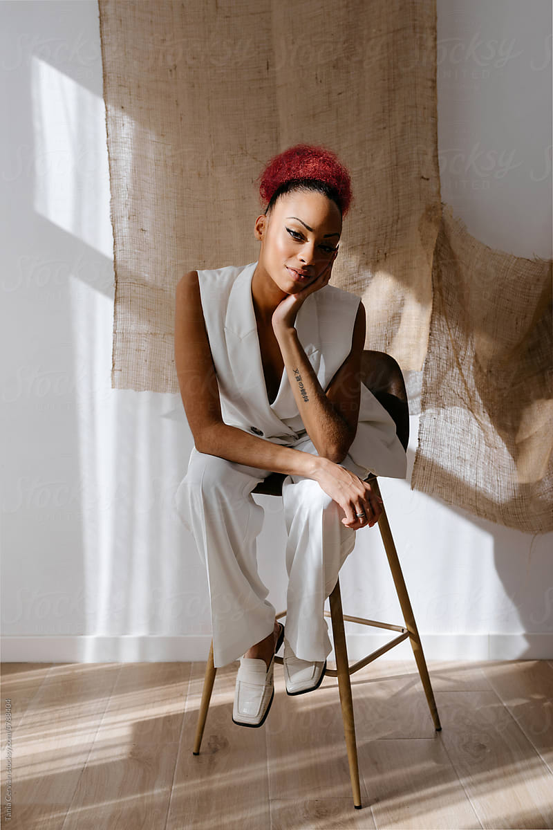 Stylish young African American woman sitting on stool in studio